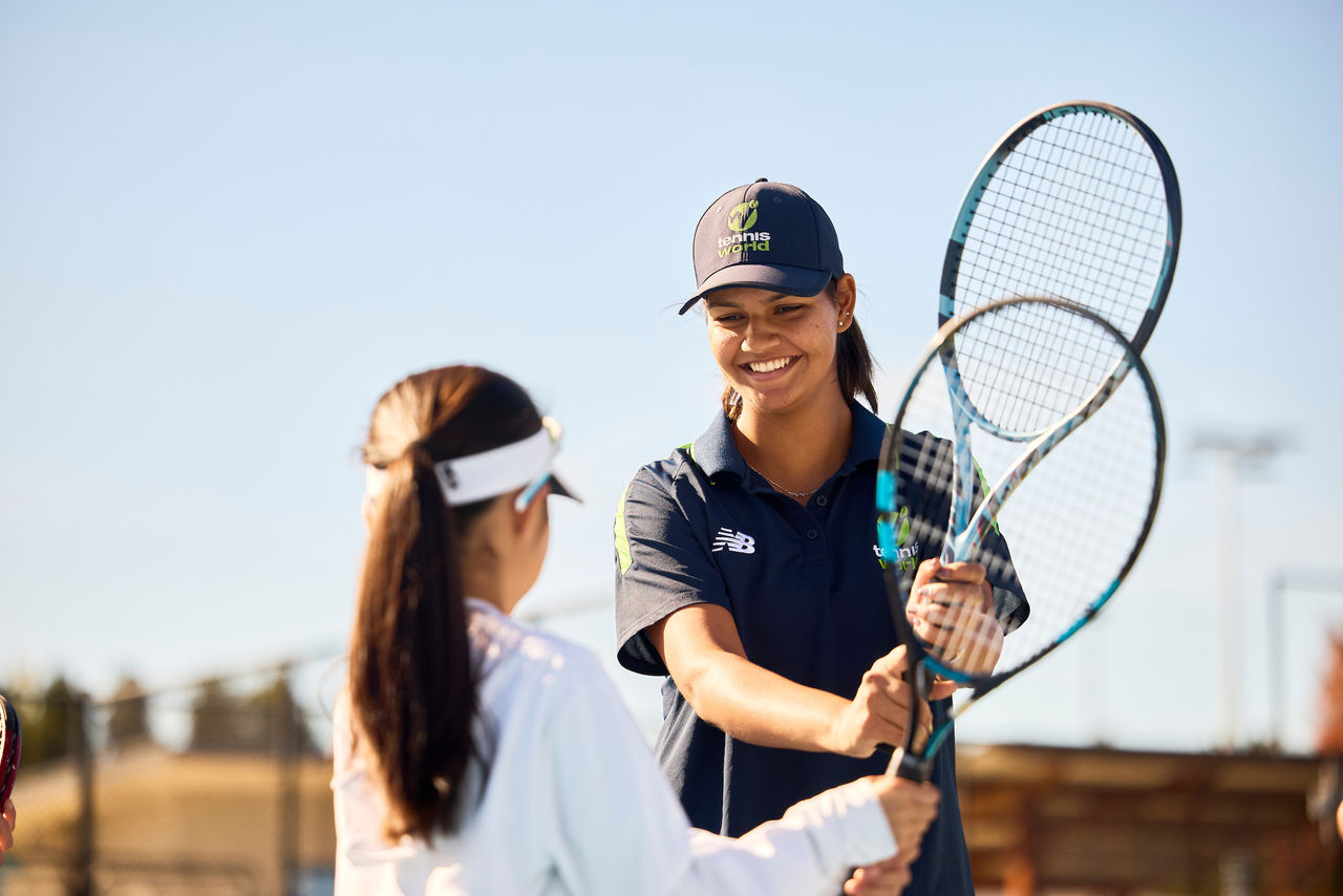 A female coach demonstrating backhand grip to a young student.